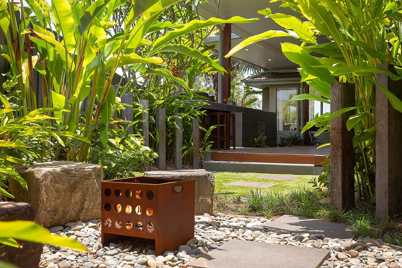 Golden cane palm canopy over a corten cube seat on a gravel path