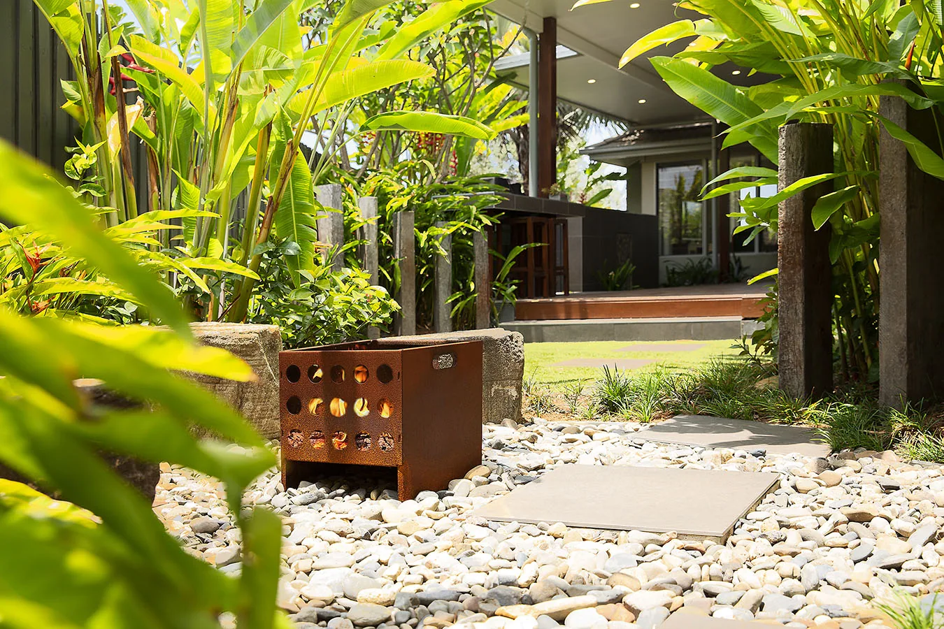Corten steel cube seat set among river pebbles and palms in a private courtyard